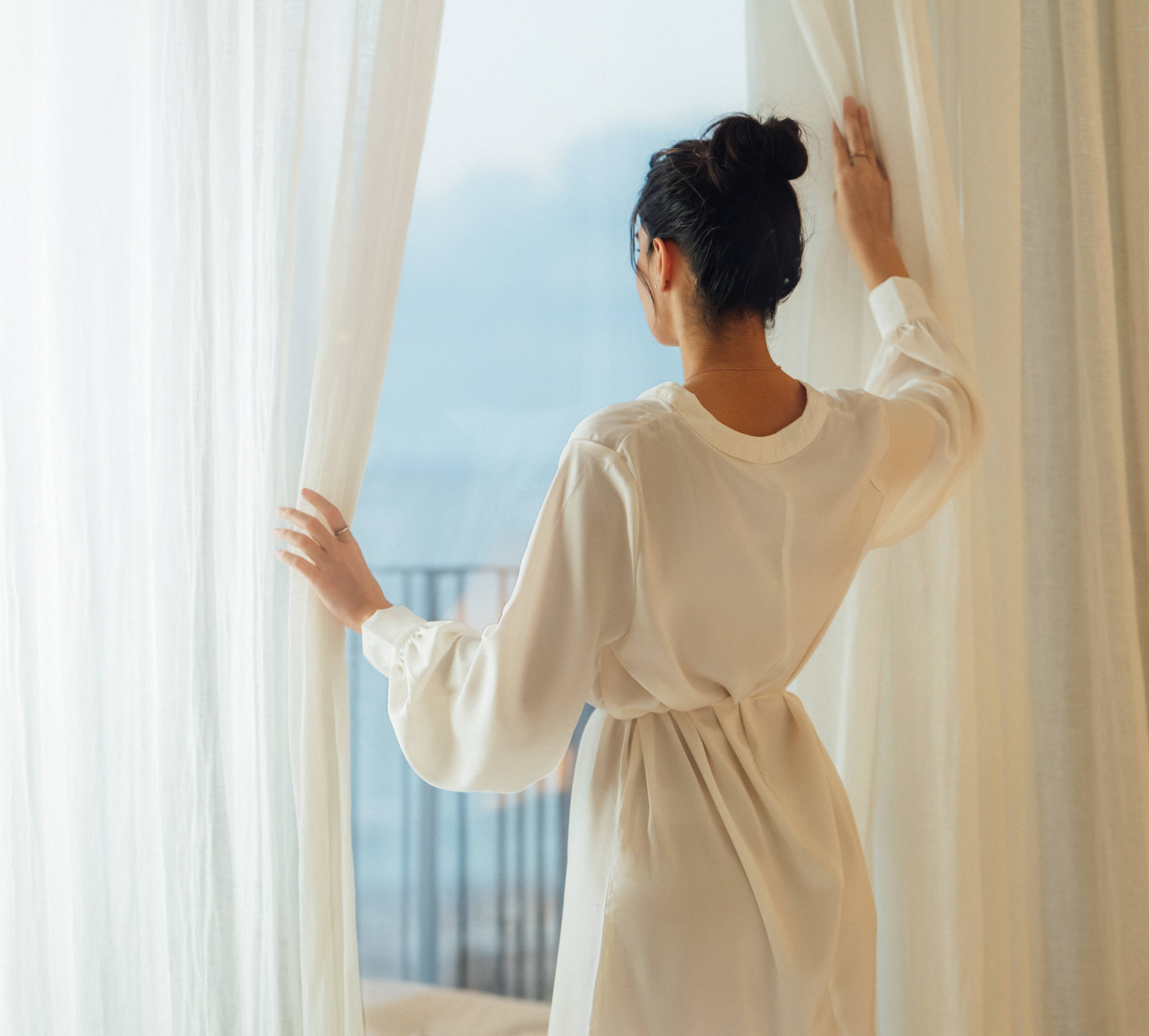 Schöne Frau öffnet die Vorhänge und geniesst die schöne Aussicht aus dem Hotelzimmer